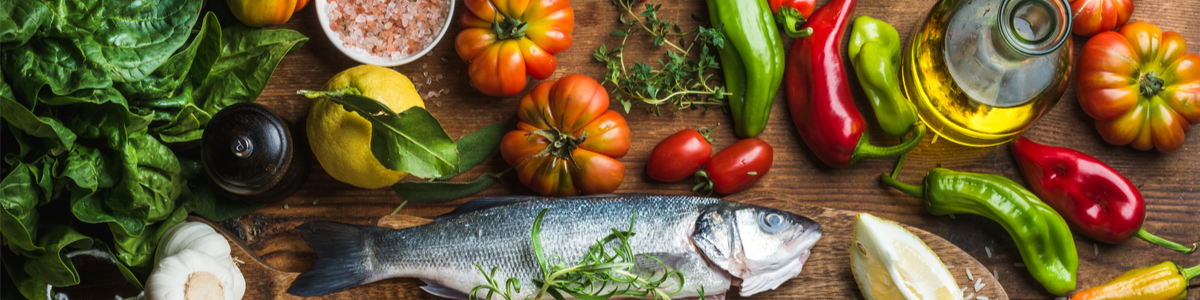 Saftige Tomaten, frischer Salat, knackige Peperoni, gesundes Olivenöl und frischer Fisch, auf einer Holzplatte appetitlich angeordnet